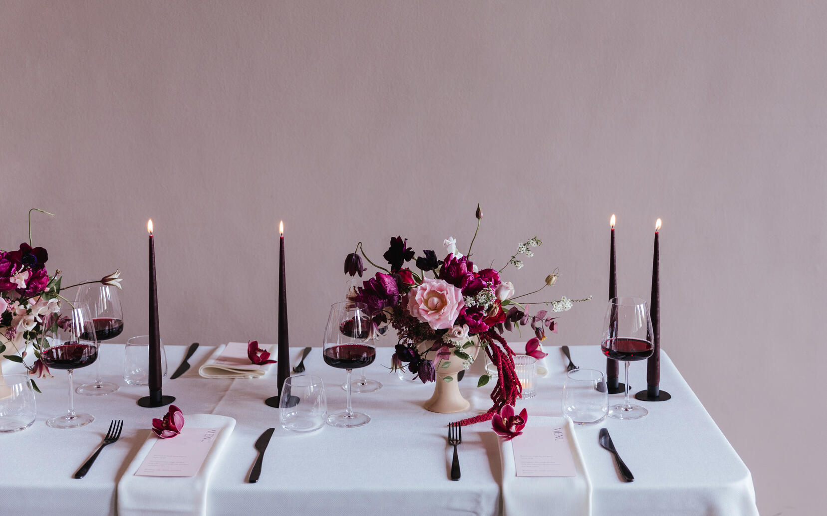 Dining table with pink flowers, purple dinner candles, stationery and glasses of red wine Dining table with pink flowers, purple dinner candles, stationery and glasses of red wine